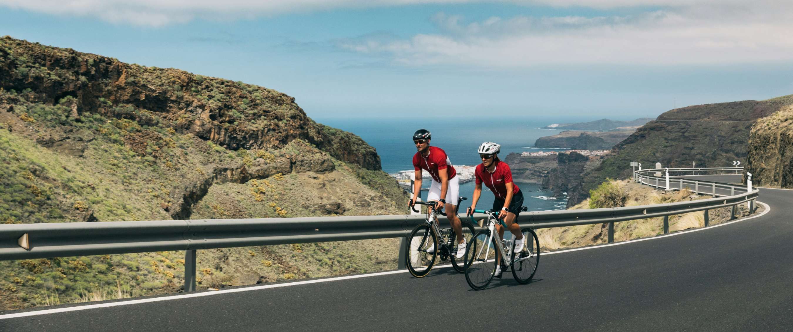 Deux cyclistes montent une route de montagne avec vue sur la mer.