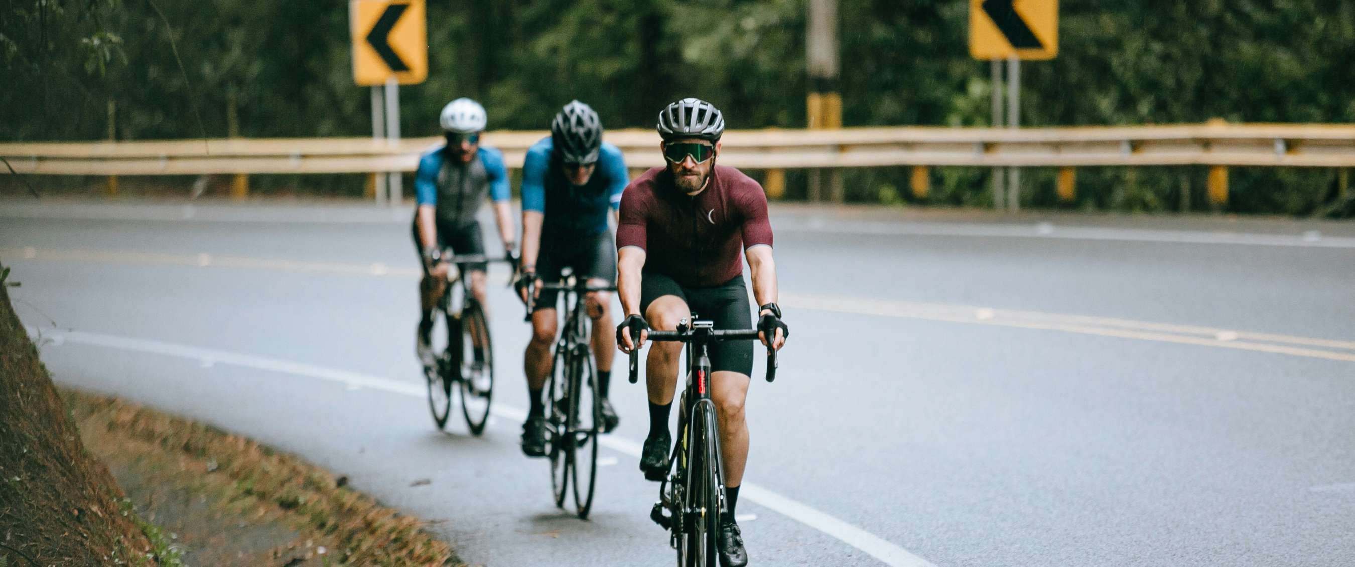 Trois cyclistes roulent en groupe dans un virage sur route mouillée.