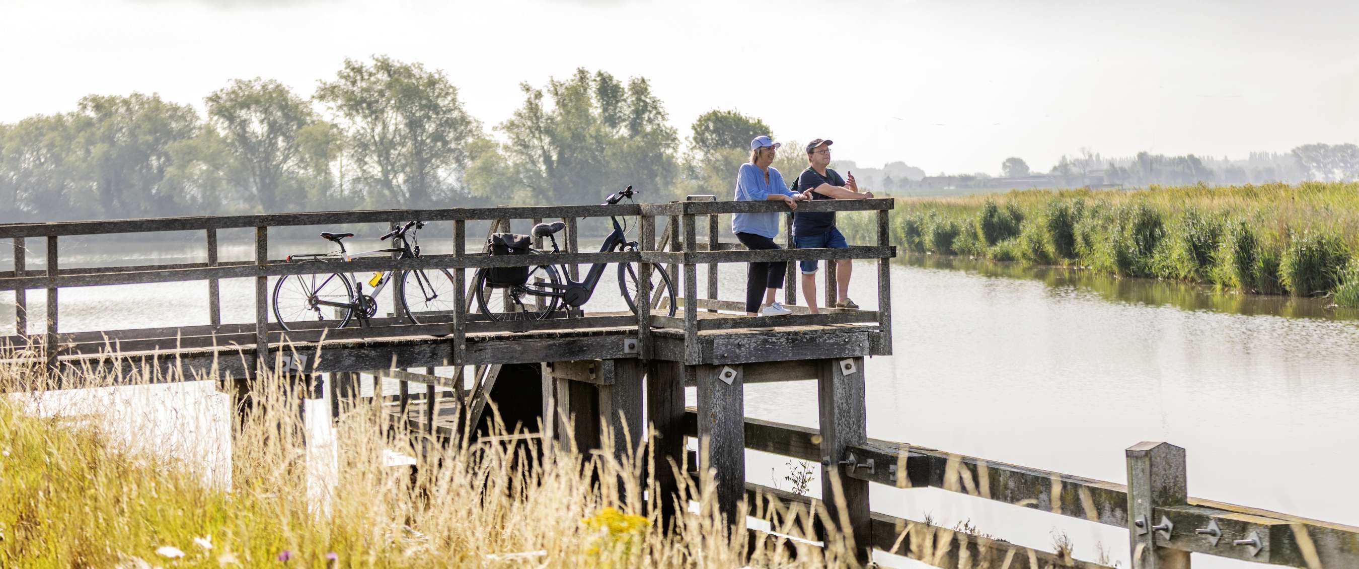 Fietsers pauzeren op een houten uitkijkplatform bij een waterrijk landschap.