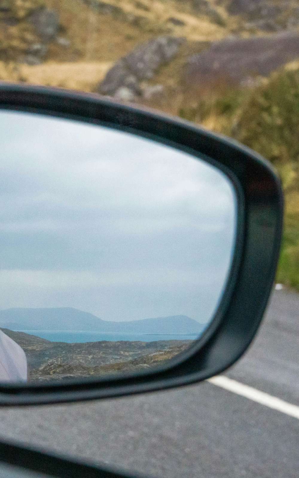 Rétroviseur avec vue nette sur la côte, la mer et les collines le long d’une route.