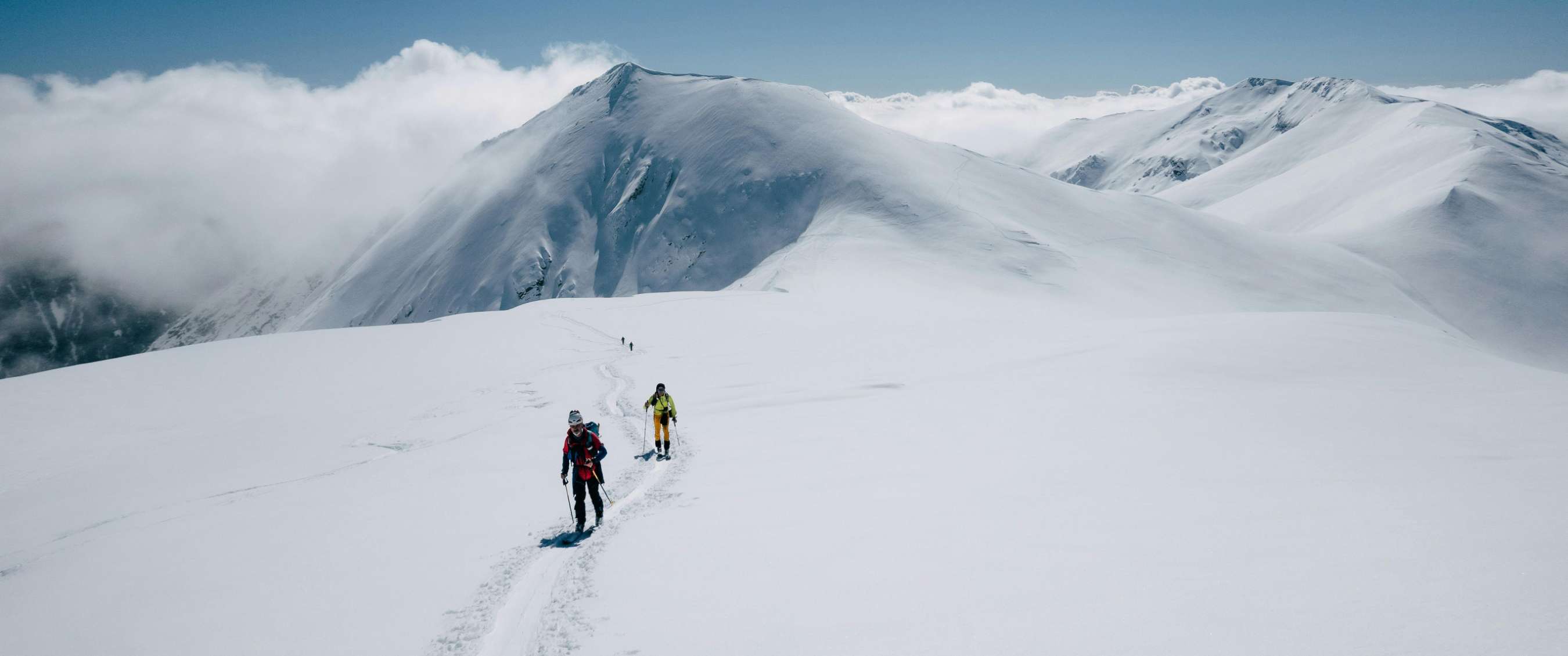Photo < Groupe de randonneurs équipés de raquettes progresse sur un vaste paysage de montagne enneigée avec sommets en arrière-plan >