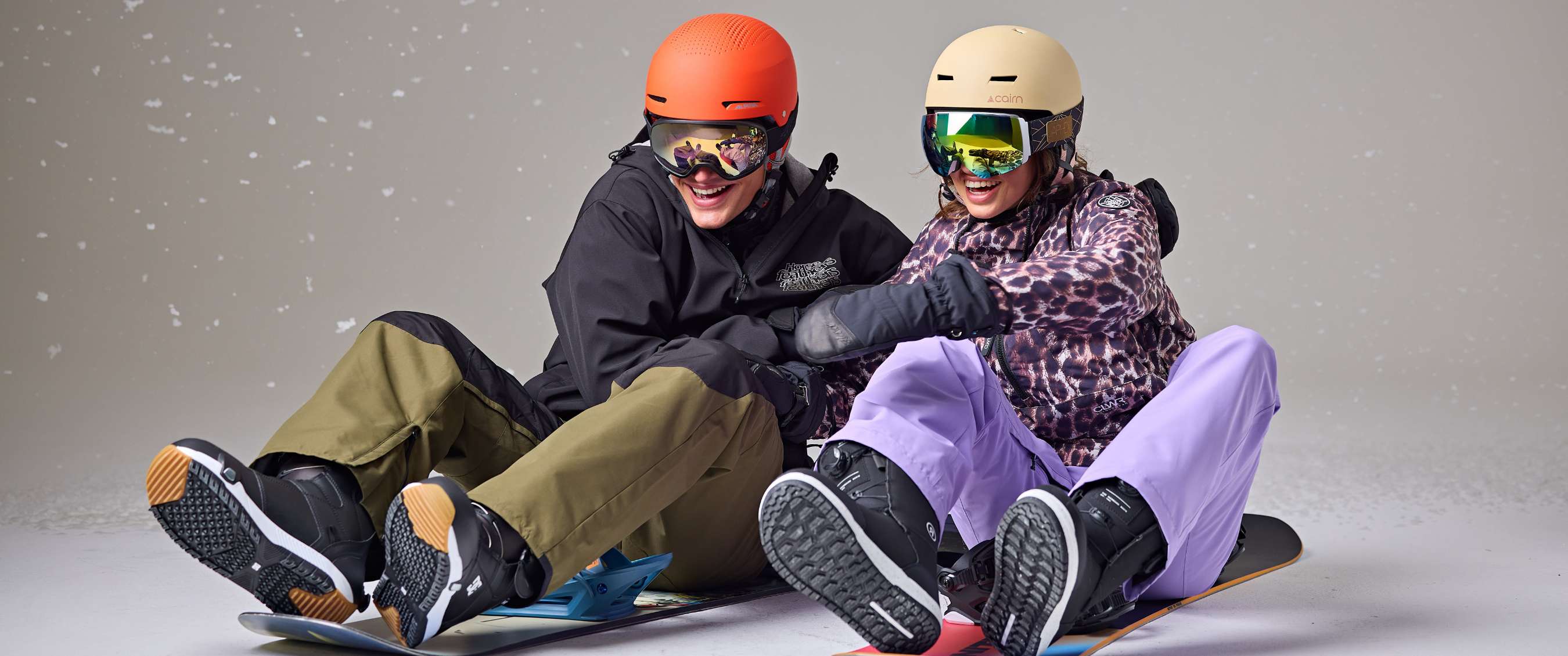 Deux snowboardeurs assis et riant dans un studio avec effet de neige.